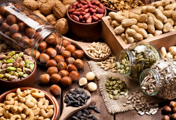 Horizontal shot of a rustic wood table filled with a large assortment of nuts like pistachios, hazelnut, pine nut, almonds, pumpkin seeds, sunflower seeds, peanuts, cashew and walnuts. Some nuts are in brown bowls and others in glass jars. Predominant color is brown. DSRL studio photo taken with Canon EOS 5D Mk II and Canon EF 100mm f/2.8L Macro IS USM